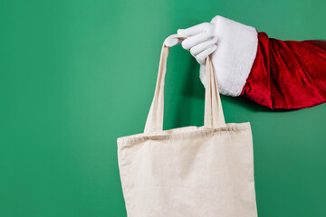 Trendy string bag in Santa's hands on green background. Sale, contactless, holidays concept. - Powered by Adobe