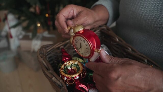 Close-up of woman's hands decorating Christmas tree wist antique clock toy