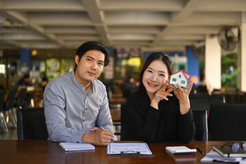 Two young real estate agents sitting in office and smiling to camera.