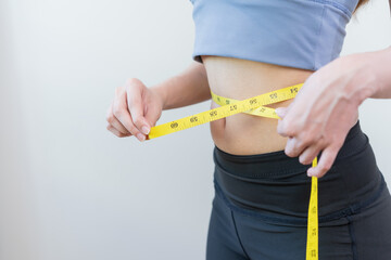 Workout, Slim asian young woman, girl standing, hand in measuring tape around waist her in fit sportswear on white background. Sport strong person in gym fitness for wellbeing, health and copy space.