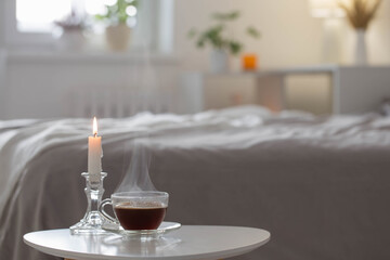 glass cup of coffee with burning candle  on white table in bedroom