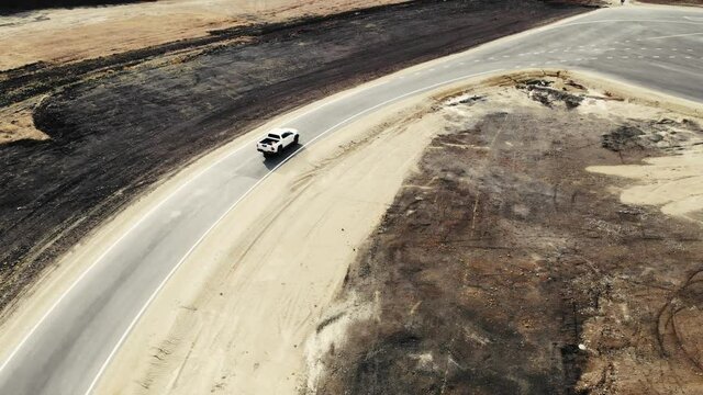 Aerial view of pickup truck that drives along track of proving ground. Driver of car checks quality of new road. Trucks and workers are standing nearby. Asphalt with road markings. Road construction