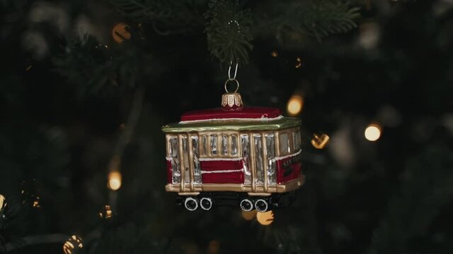 Close-up of woman's hands decorating Christmas tree with toy of retro tram 