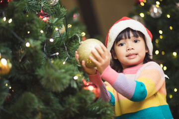 Asian child hanging decorative toy ball on Christmas tree branch