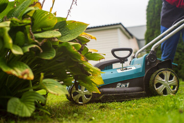 Happy retired senior person mows a lawn in his garden with a lawnmower. Mulching the grass at...