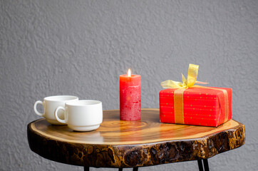Gift. Present in red packaging. Gold bow. Christmas and New Year. A candle is burning. Valentine's day. There are two cups on the table. Coffee.