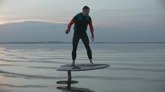 Man riding on a hydrofoil surfboard on large blue lake at the pink sunset. Shot of man riding a hydrofoil surfboard in the middle of the lake. High quality 4k footage