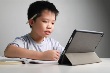 Portrait of a little Asian boy using tablet computer during pandemic lockdown, homeschooling, social distance, stay at home, online education concept.