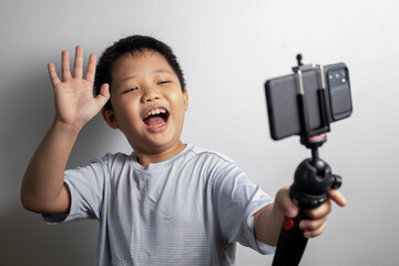 Portrait of a little Asian boy blogger talking on a smartphone front camera, making a video blog. Vlogger, social media live streaming concept.