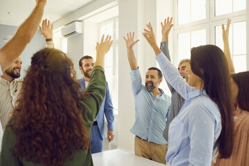 Naklejka na ściany i meble Team of happy business people celebrating success. Group of young and mature employees standing around office table, giving each other high five and raising hands up together. Teamwork concept