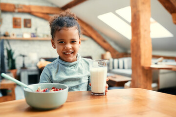 Happy black girl with milk mustache during breakfast at home.