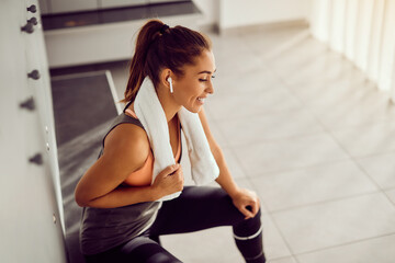 Young athletic woman listens music over wireless earphones in dressing room at gym.