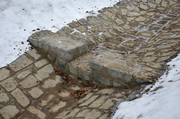 Sewer gutter paved with granite stone and dikes drains rainwater by ditch at the highway into the retention reservoir where the water slows down to the sewer through a pipe with a drain grid