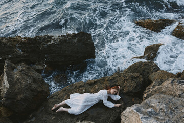 beautiful woman in a secluded spot on a wild rocky coast in a white dress view from above