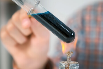 Closeup of test tube with liquid burning on alcohol lamp, chemistry experiment. The liquid boils,...