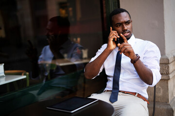African businessman drinking coffee in cafe. Happy smiling man talking to the phone.