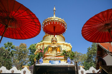 The golden Buddha statue is located in front of the pagoda. with an altar in front and an ancient red umbrella on either side.