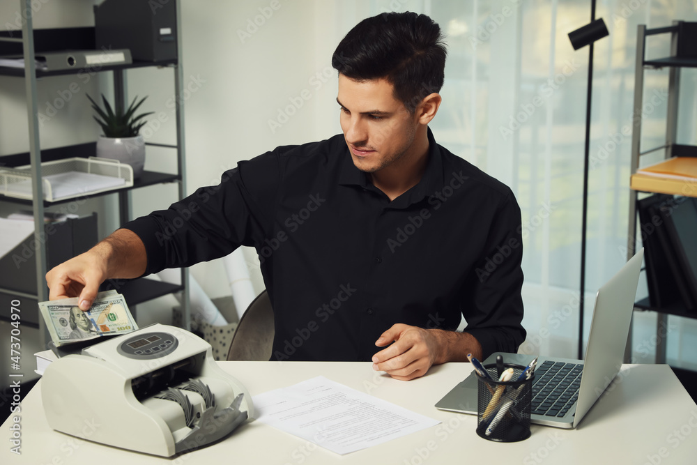 Wall mural Man putting money into banknote counter at white table indoors