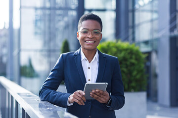 Successful business woman smiling and happy enjoys tablet computer during break, african american woman at office outside