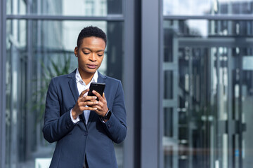 thinking business woman using phone, african american woman in business suit near office concentrated