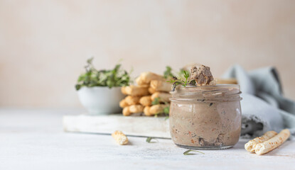 Homemade liver pate, spread or mousse in glass jar with grissini and microgreens, light concrete background.