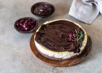 Classic creamy cheesecake with chocolate ganache, cherries and rosemary on concrete background. Popular festive dessert.