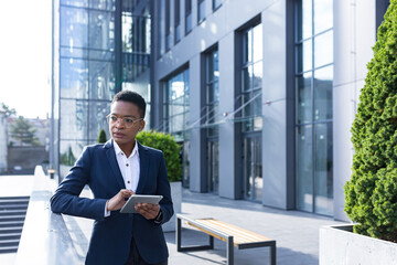 Fototapeta premium Serious and thinking business woman African American on a break near the office, uses a tablet online, reads statistics uses the application