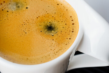 Close up photo of fresh espresso with foam in white cup, top view from above