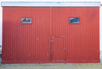 Very tall old red barn door with two small windows and a door