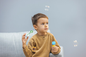 Boy playing soap bubbles. Cute little boy at home blowing bubbles. Three years old child boy blowing bubbles. Happy childhood. Positive. Little boy with soap bubbles on grey background