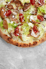 Delicious pizza Caesar style with white sauce, chicken, parmesan, egg, cherry tomatoes and fresh lettuce at wooden background. Restaurant pizzeria menu with delicious taste pizza Caesar.