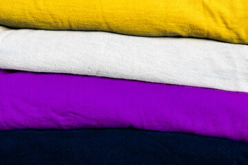 A stack of clothes folded in the colors of the nonbinary community flag. Background with place for text for a template on the theme of tolerance and gender diversity