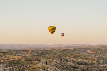 Cappadocia, Turkey - 21 July 2021: Colorful hot air balloon flying over white mountains. Hot air balloons flying in sunrise sky. Goreme mountains scenic view