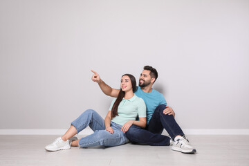 Young couple sitting on floor near light grey wall indoors