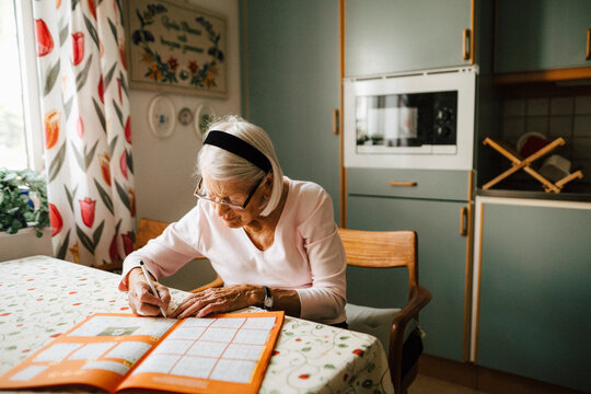 Senior woman solving sudoku at dining table in kitchen