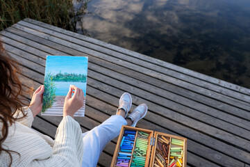 Woman drawing with soft pastels on wooden pier near river, closeup