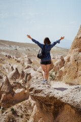 Young happy woman with backpack among mountains with raised hands enjoying the view