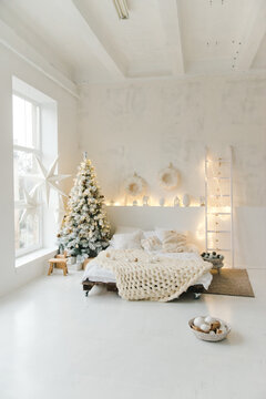 Light cozy bedroom decorated for celebrating Christmas. Eco style interior in white colors with tender pind linen on a bed. Xmas in a bed room. Christmas concept. Bedroom in christmas interior.