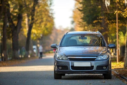Modified image of a fictional non existent car. Car parked in quiet area on asphalt road on blurred green and yellow trees bokeh background on bright sunny day. Transportation and parking concept.