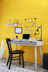Stylish home office interior with comfortable workplace near yellow brick wall