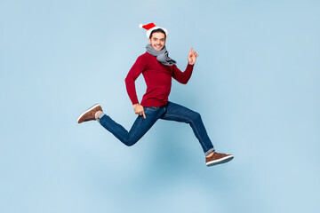 Naklejka na ściany i meble Young handsome Caucasian man in Christmas outfit jumping with hands pointing up and down in isolated color light blue background