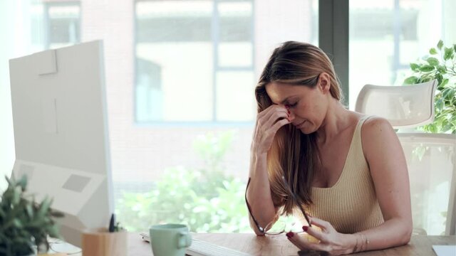 Video of tired business woman with headache looking uncomfortable while working with computer in the living room at home.