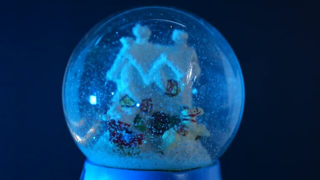 Christmas glass snow globe with Santa Claus, a reindeer and a house inside, with moving snow, with reflected colored lights. Christmas, Santa and celebration concept.