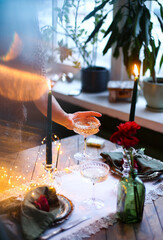 Glasses of sparkling champagne and candles at romantic Christmas table setting. Lifestyle fine dining holidays concept. Blurred female on the background. Festive meal table decoration in soft focus.