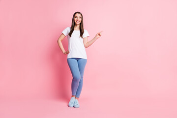 Full length body size photo girl curious in stylish outfit smiling pointing copyspace isolated pastel pink color background