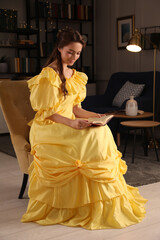 Beautiful young woman in yellow dress reading book at home