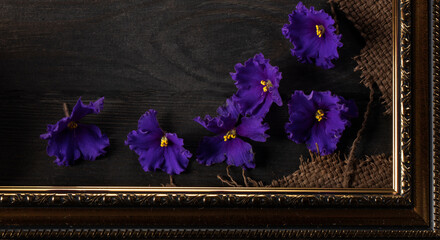 Part of a beautiful frame contains rough weave fabric on a wooden background and violet flowers....