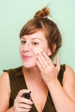Redhead Woman Applying Foundation On Her Face
