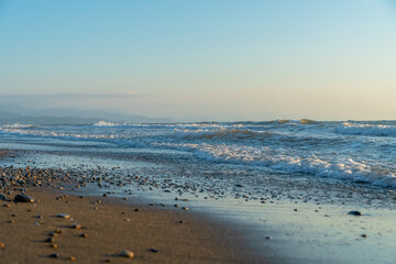 Close-up of sand and small pebbles on the beach against the background of the sea and the sky at sunset. Beautiful nature background