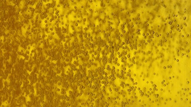 SLOW MOTION, VERTICAL, MACRO, DOF: Tiny co2 bubbles float around the golden beer getting poured into a glass. Yellow carbonated beverage bubbles inside a transparent glass. Bubbling pale ale in a mug.